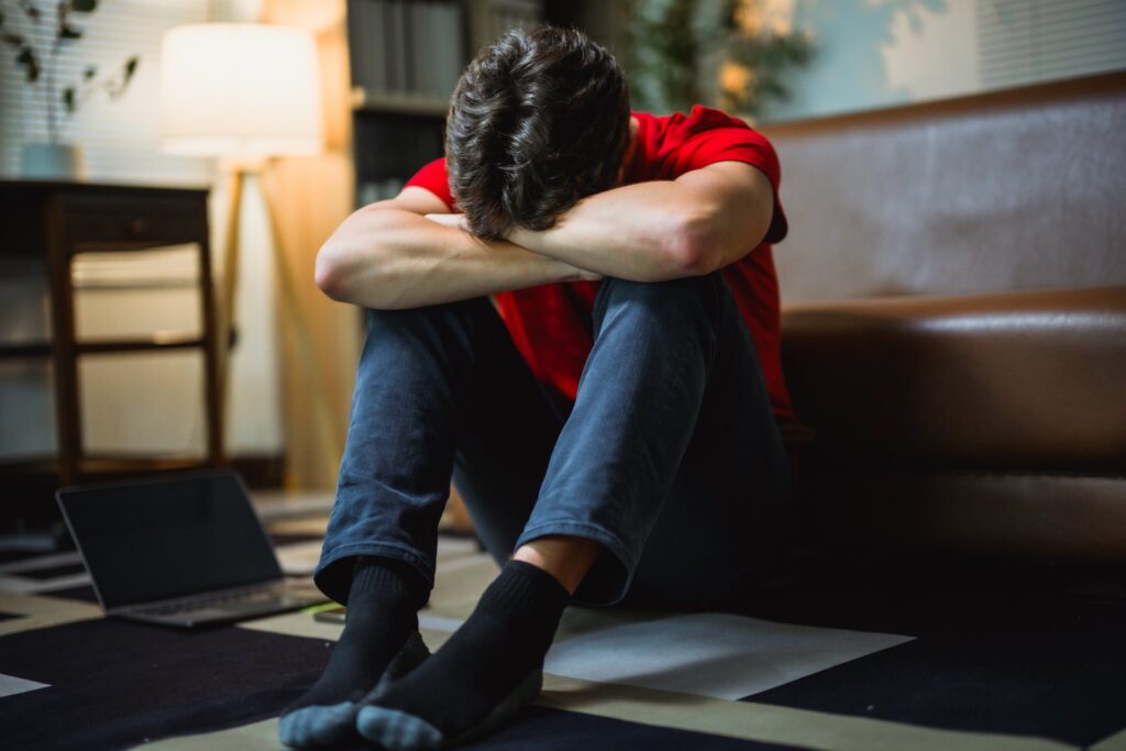 Young man sitting on floor hunched over next to a laptop