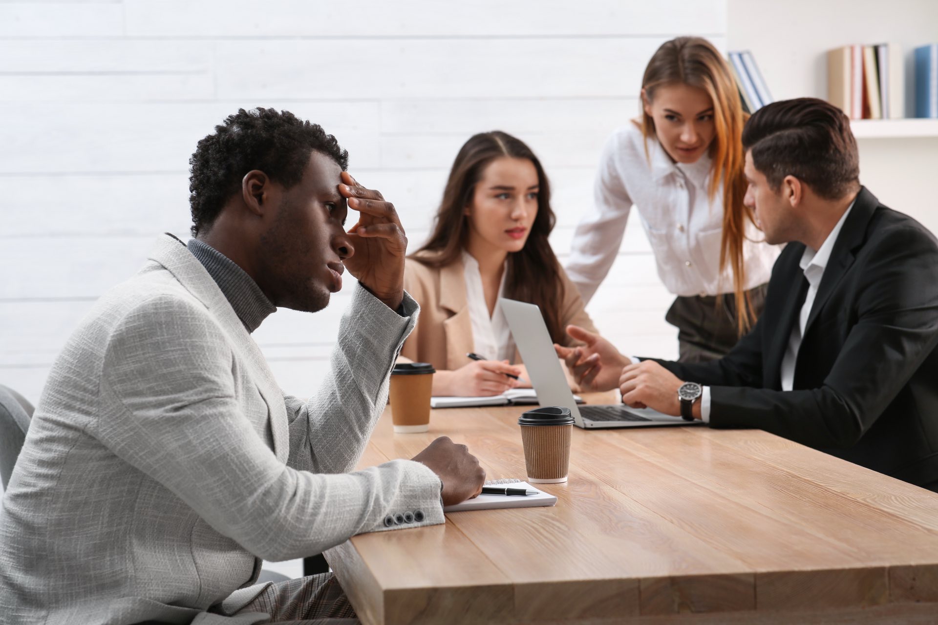 Four people sitting at a desk with three of them huddled together and one singled out