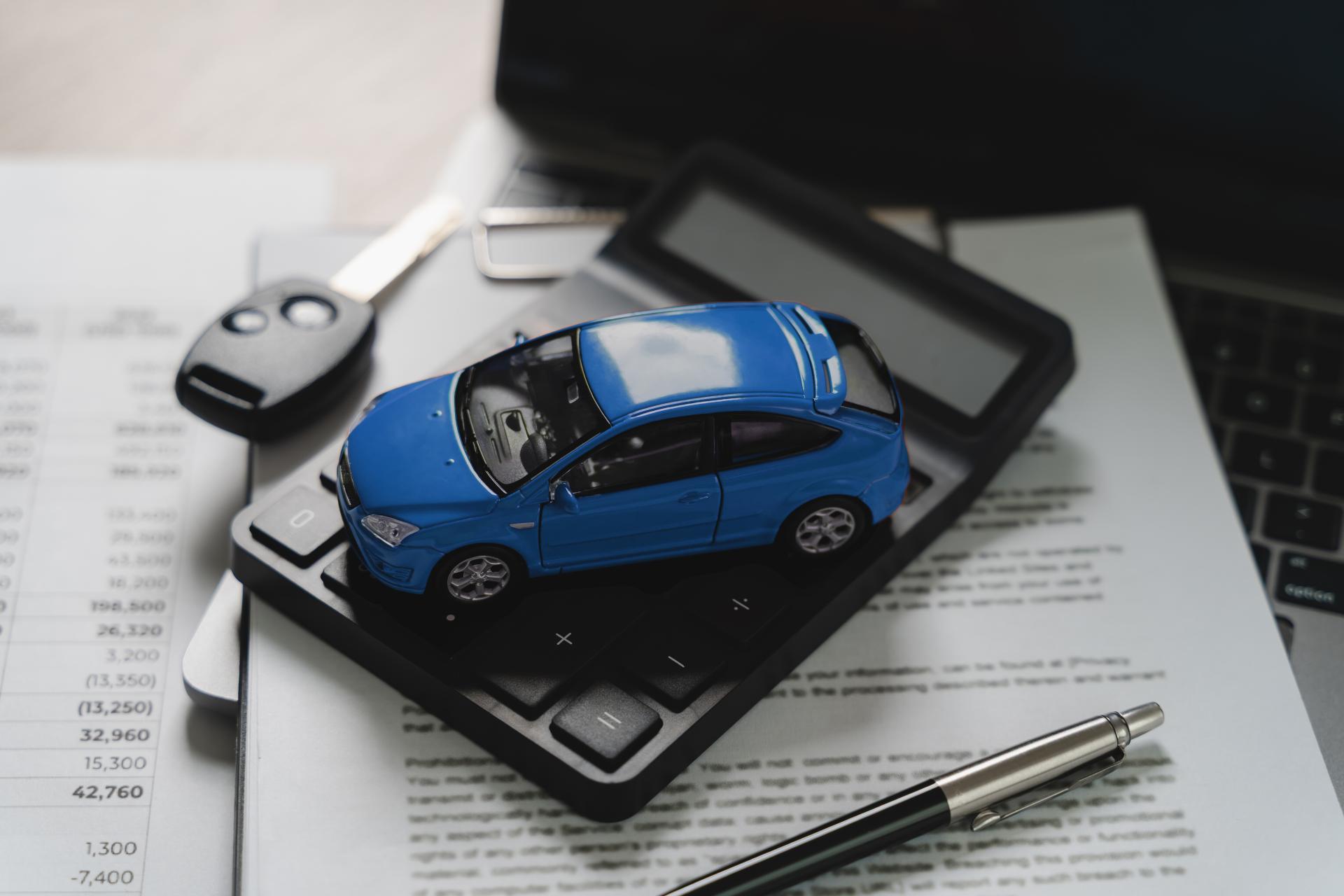 A small blue toy car sits on a calculator resting on paperwork next to a key fob.