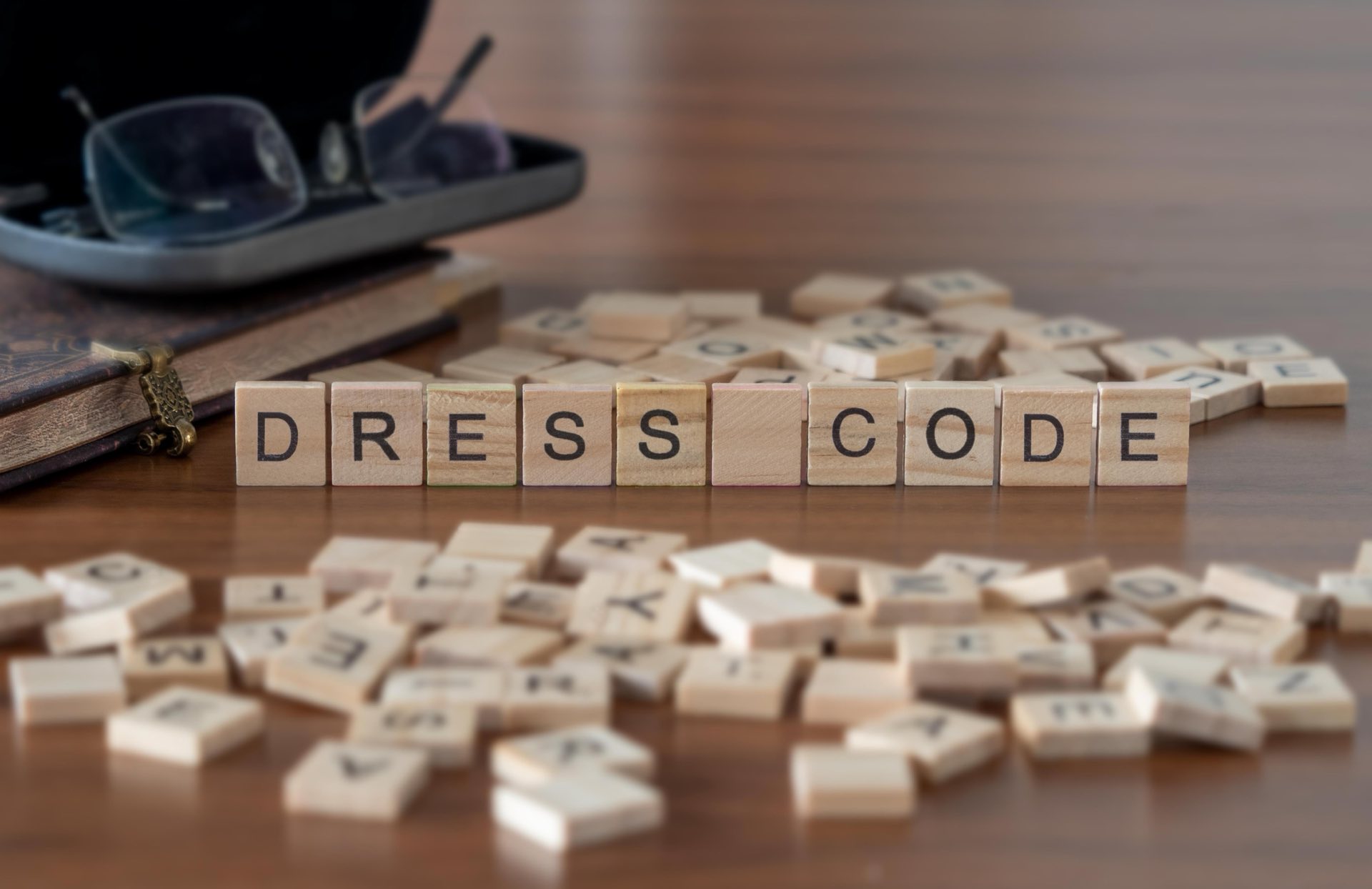 The word Dress Code in wooden blocks surrounded by wooden blocks and a book and glasses