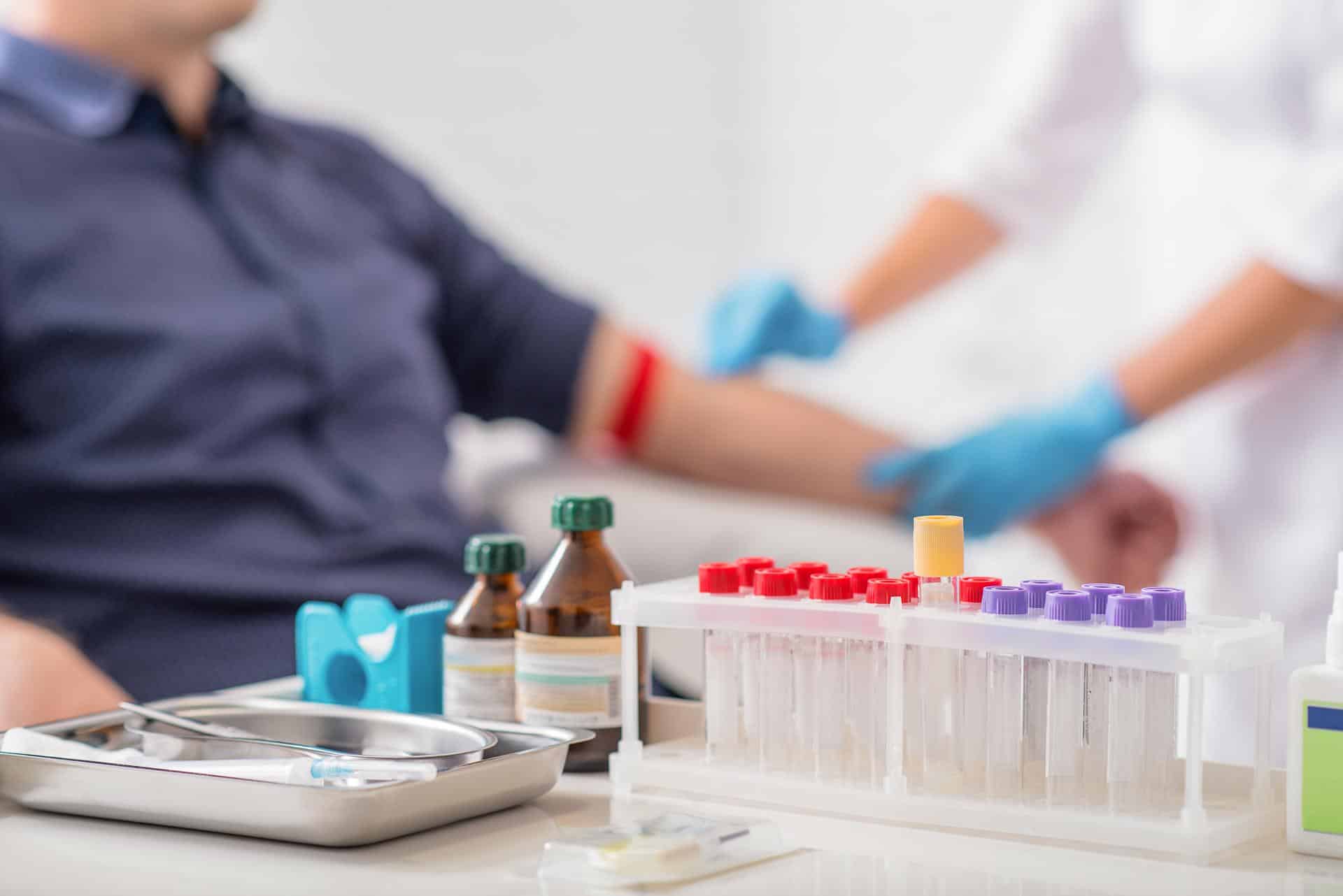 A man being prepped to get blood drawn by a nurse with vials and medical devices in the foreground.