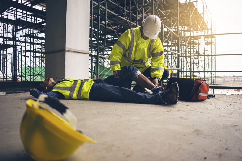 Worker administering first aid to worker at construction site