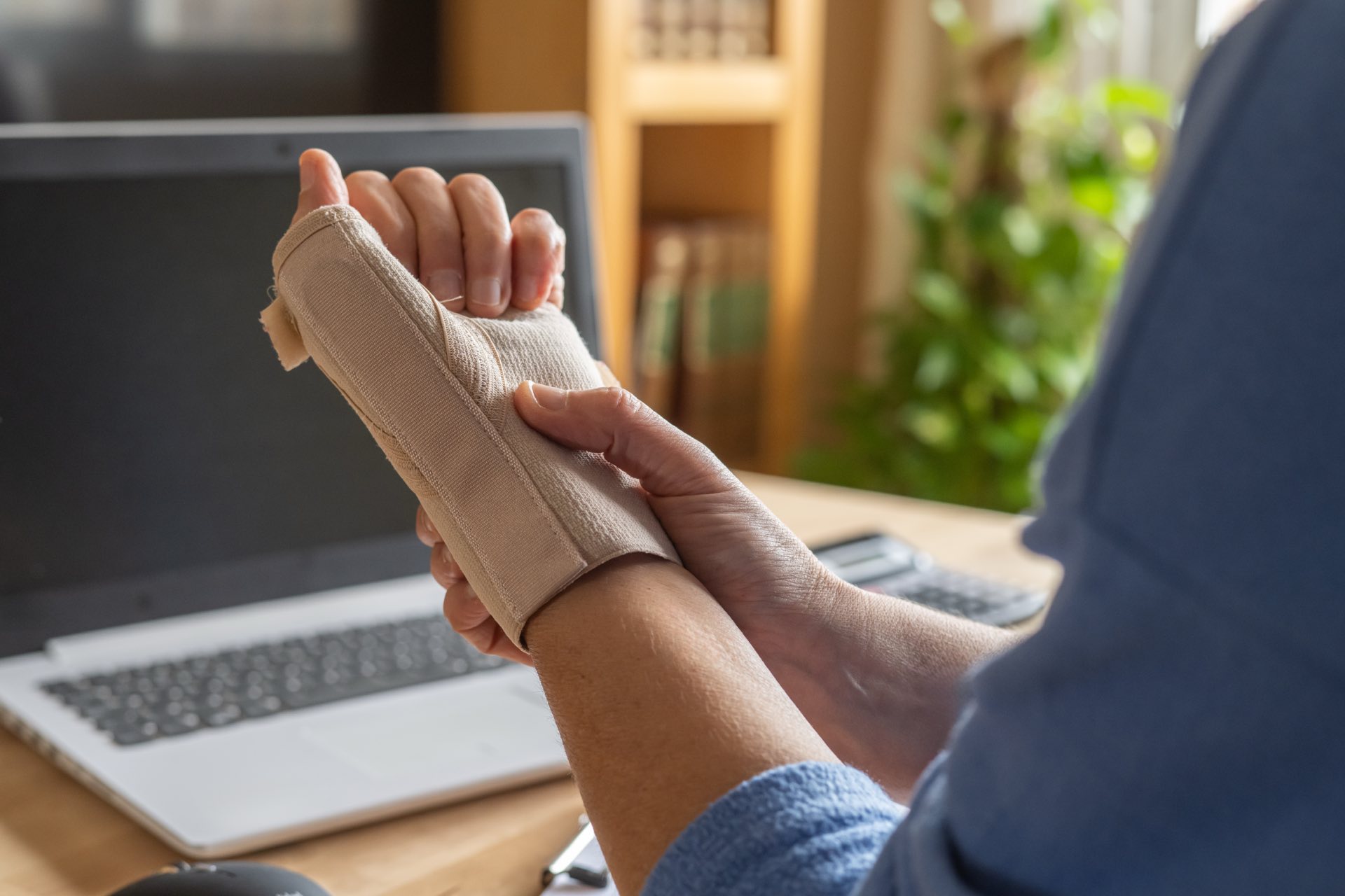 Person holding onto wrist brace with a laptop in the background