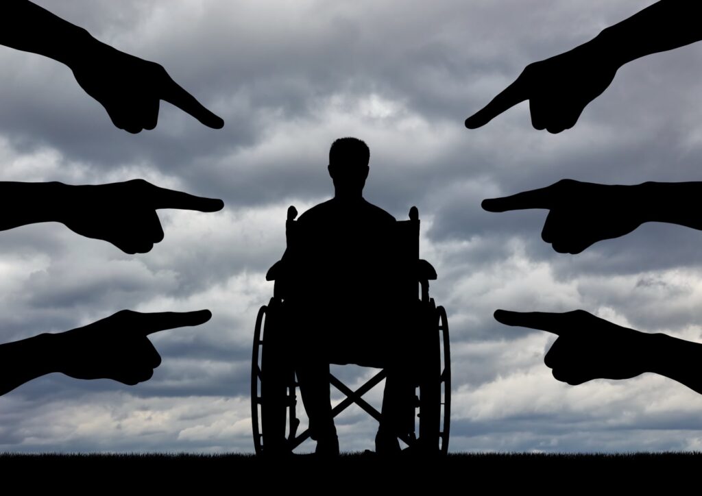 A disabled person in a wheelchair, people hands showing a finger at him.
