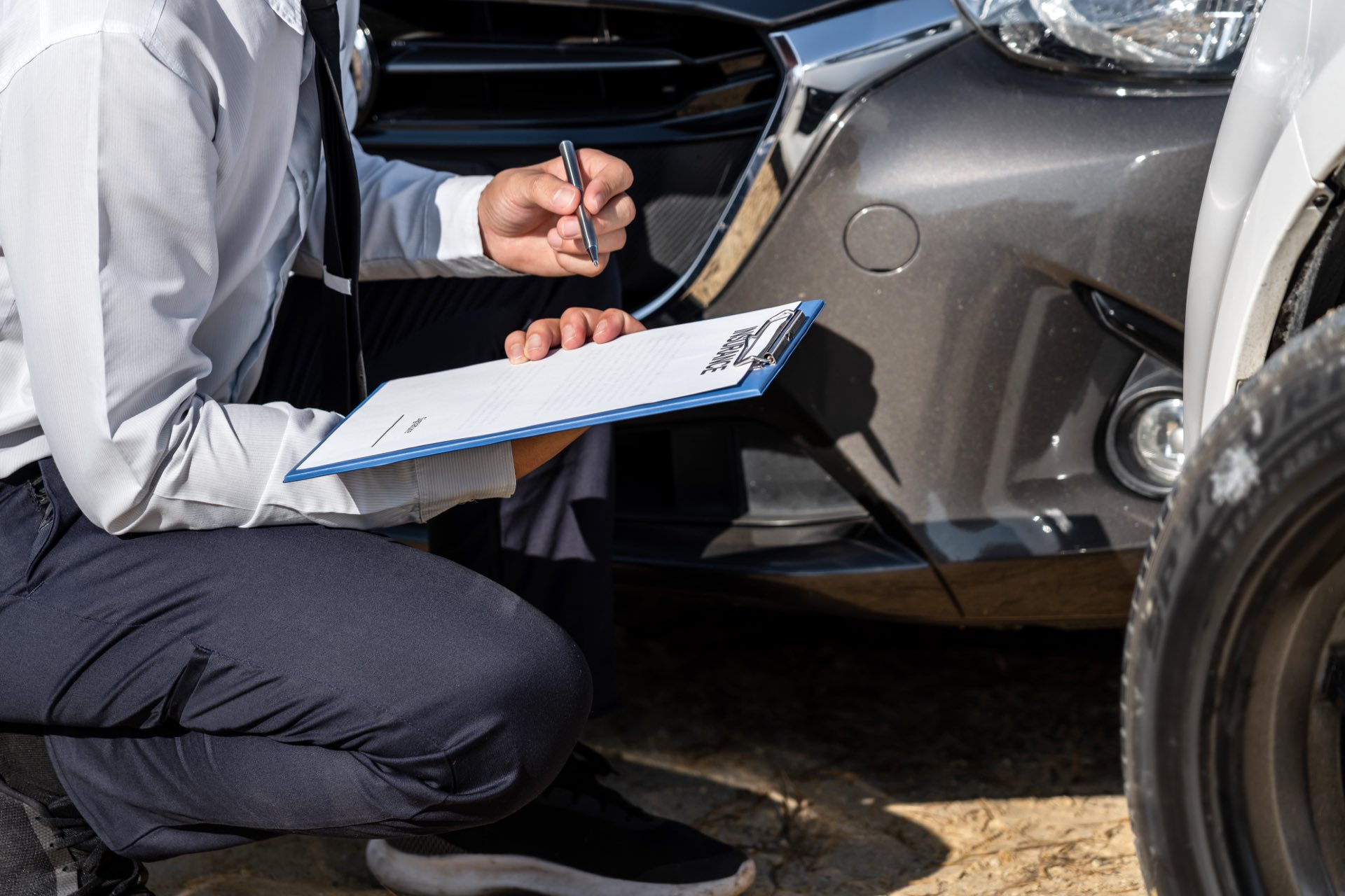 Person inspecting a car accident holding a pen and clipboard
