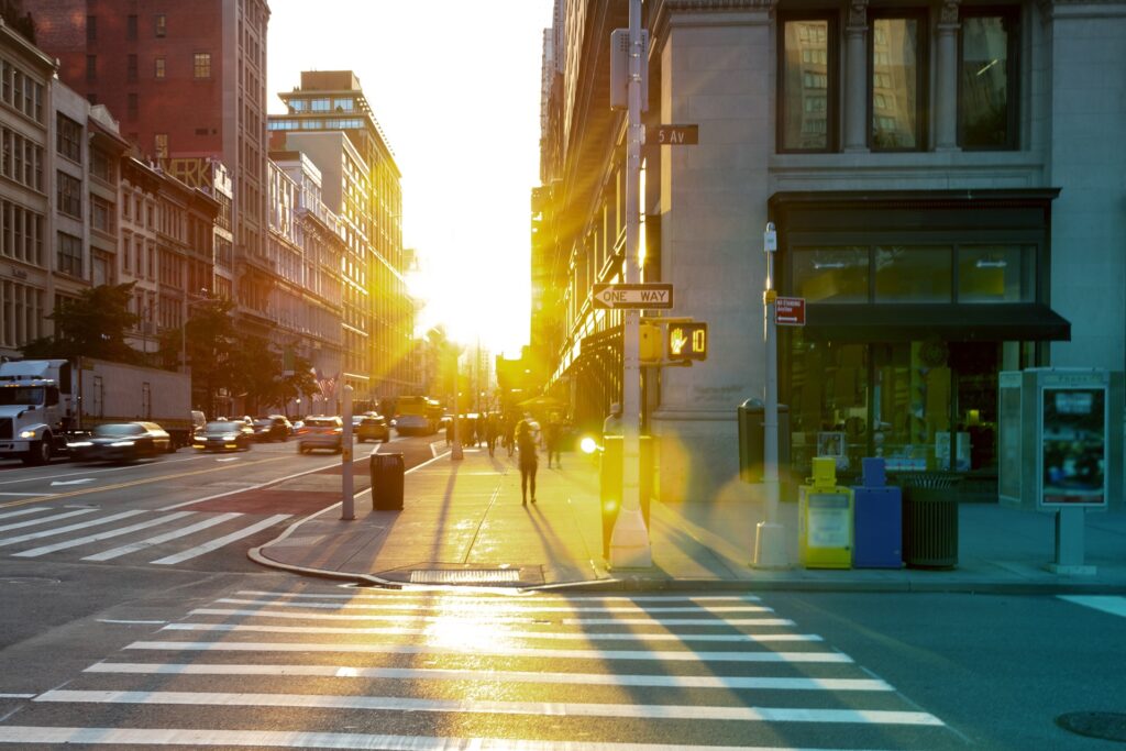 A street in downtown New York with early morning sun shining at the camera in the background.