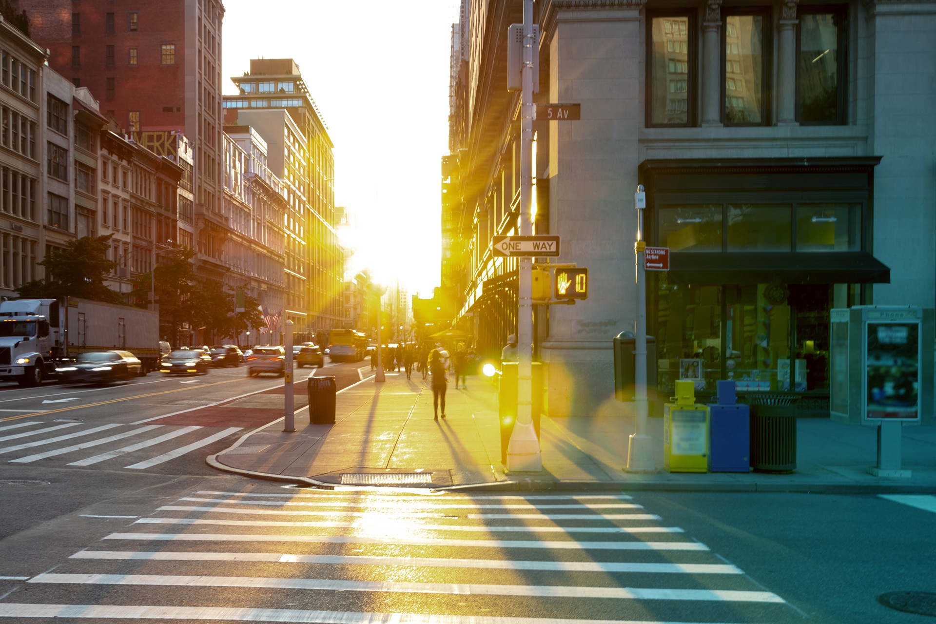 A street in downtown New York with early morning sun shining at the camera in the background.
