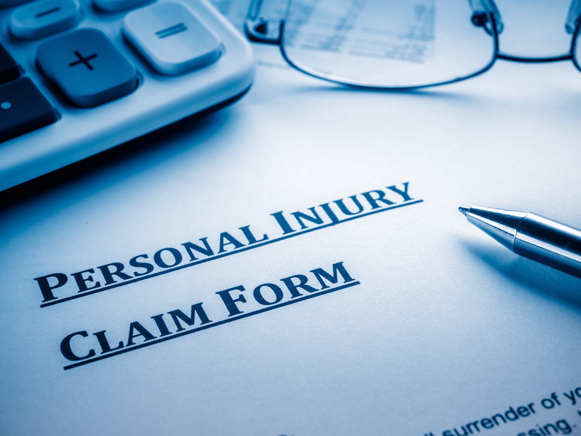 Paperwork that says personal injury claim form next to a pen, calculator and reading glasses