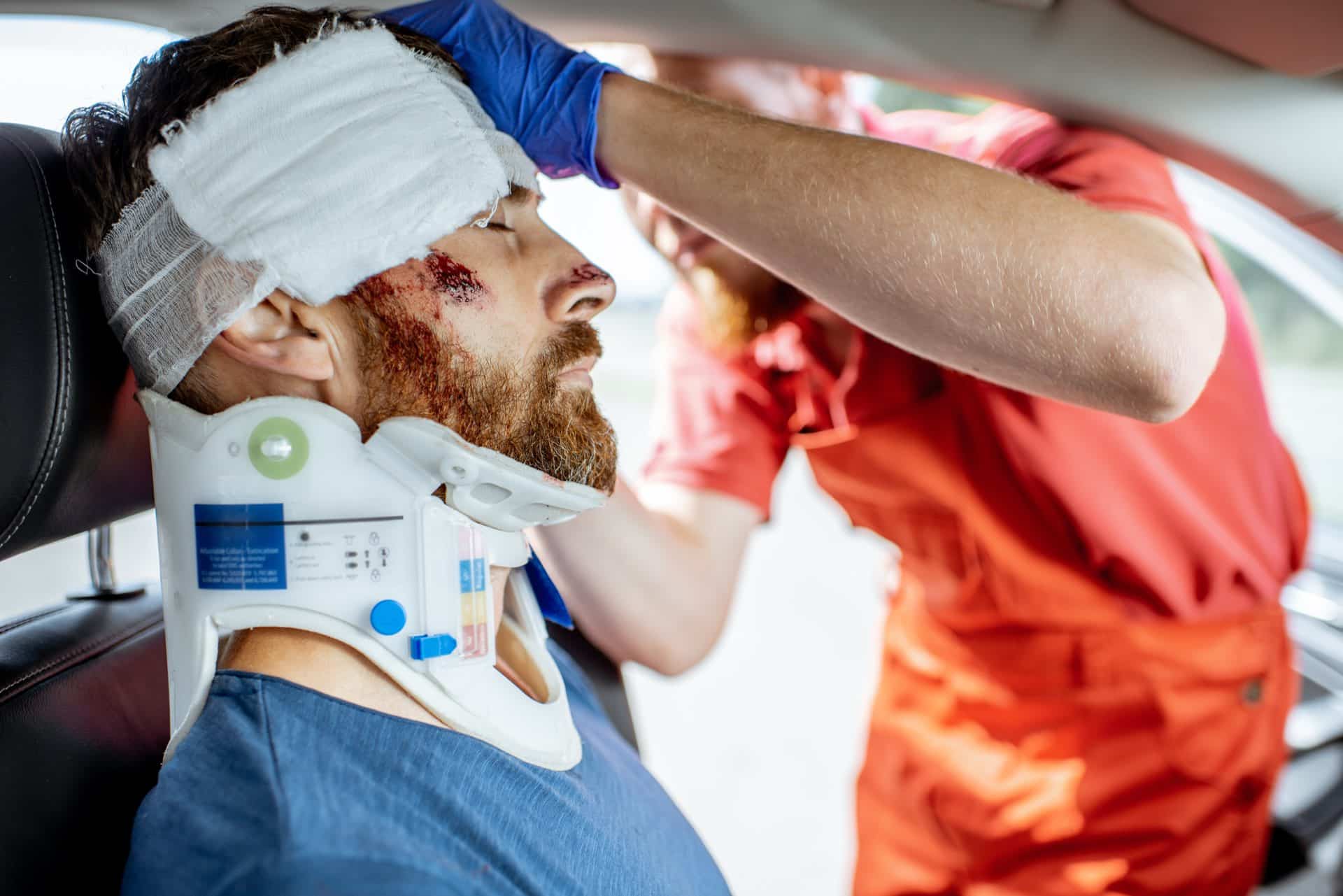 A person with a neck brace and bandage on his head and another person in an orange outfit helping him