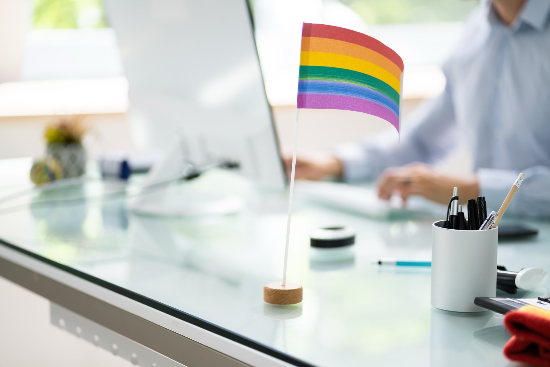 A desk with a cmoputer, pens, and a LGBT flag