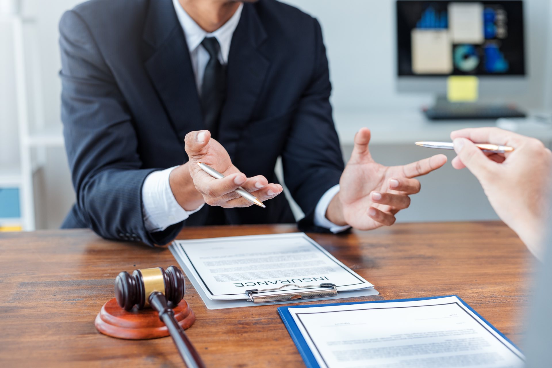 Person holding a pen at a desk with a clipboard of paperwork next to a gavel