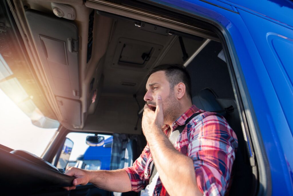 A truck driver in a blue truck who is yawning