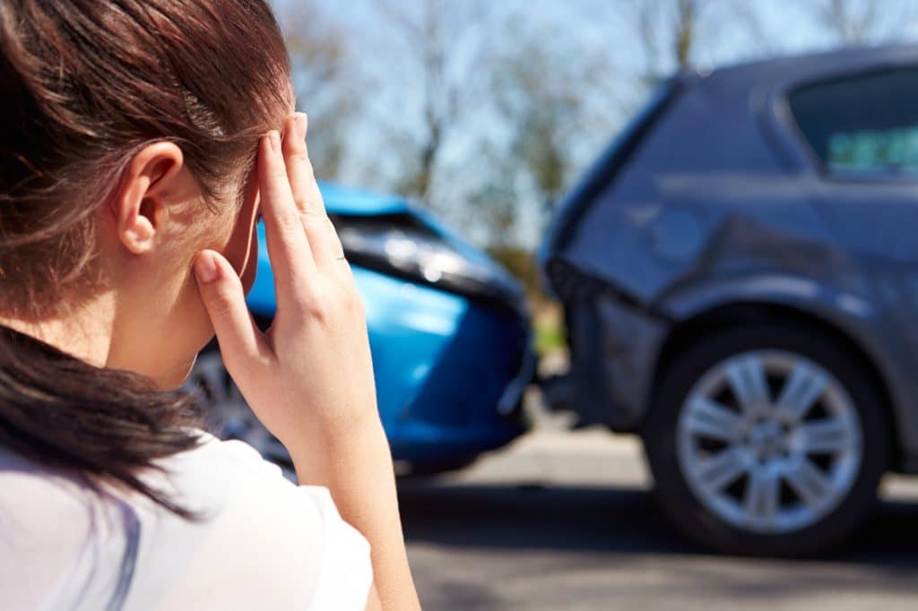 Woman with a hand to her head looking towards a rear-end car accident