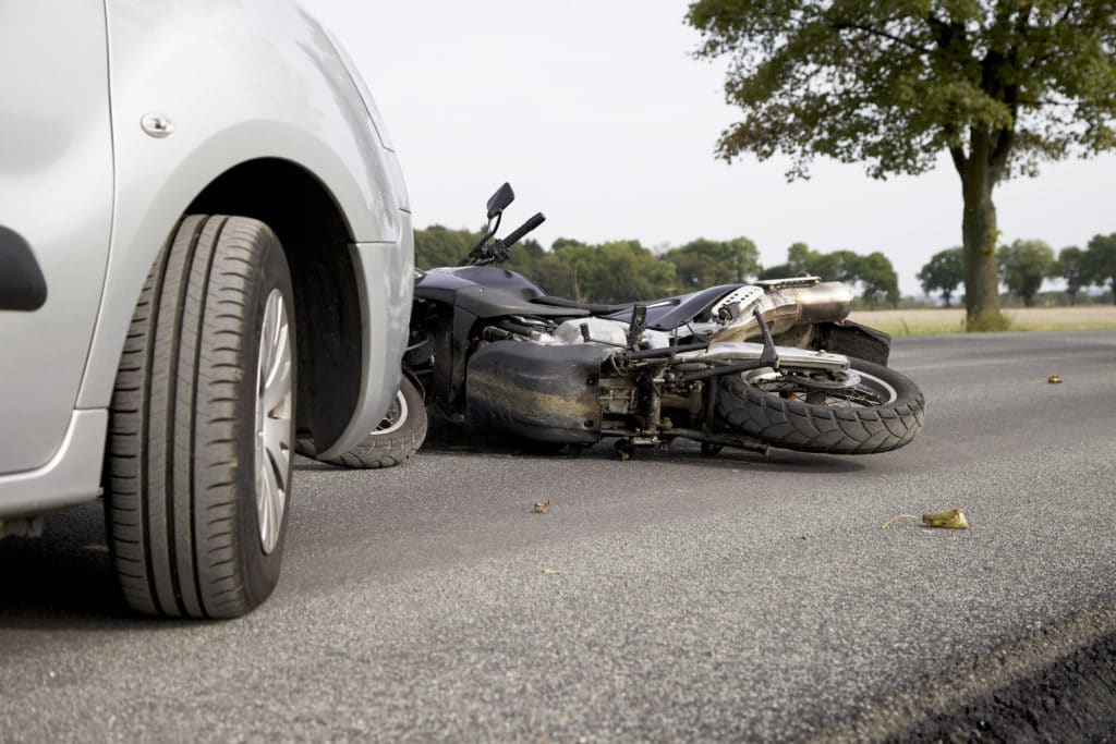 Motorcycle on its side next in front of a car on a country road