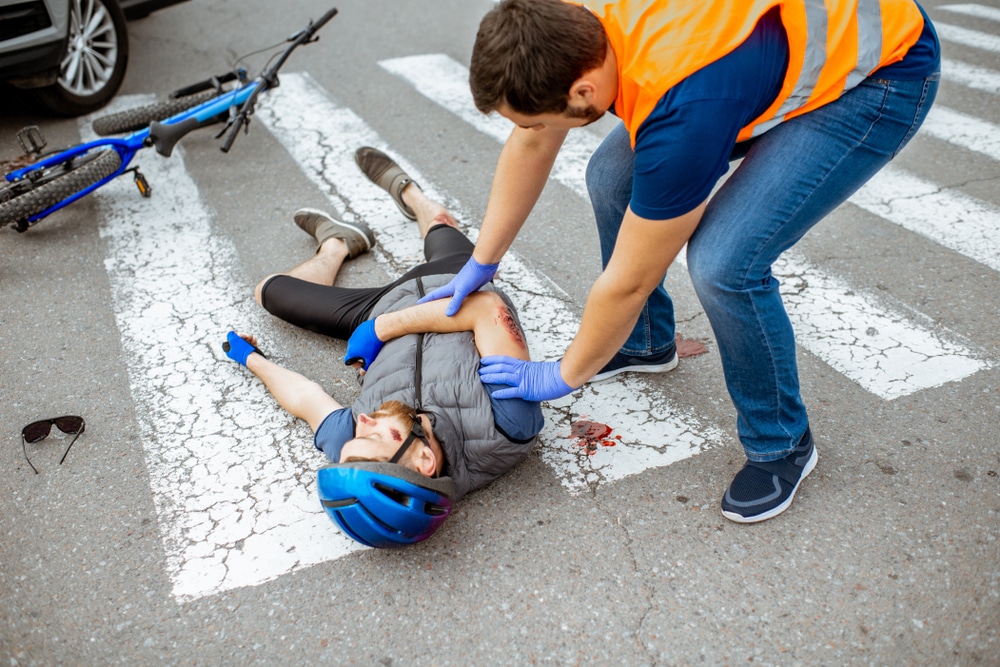 Medic tending to injured biker with bloody arm on crosswalk