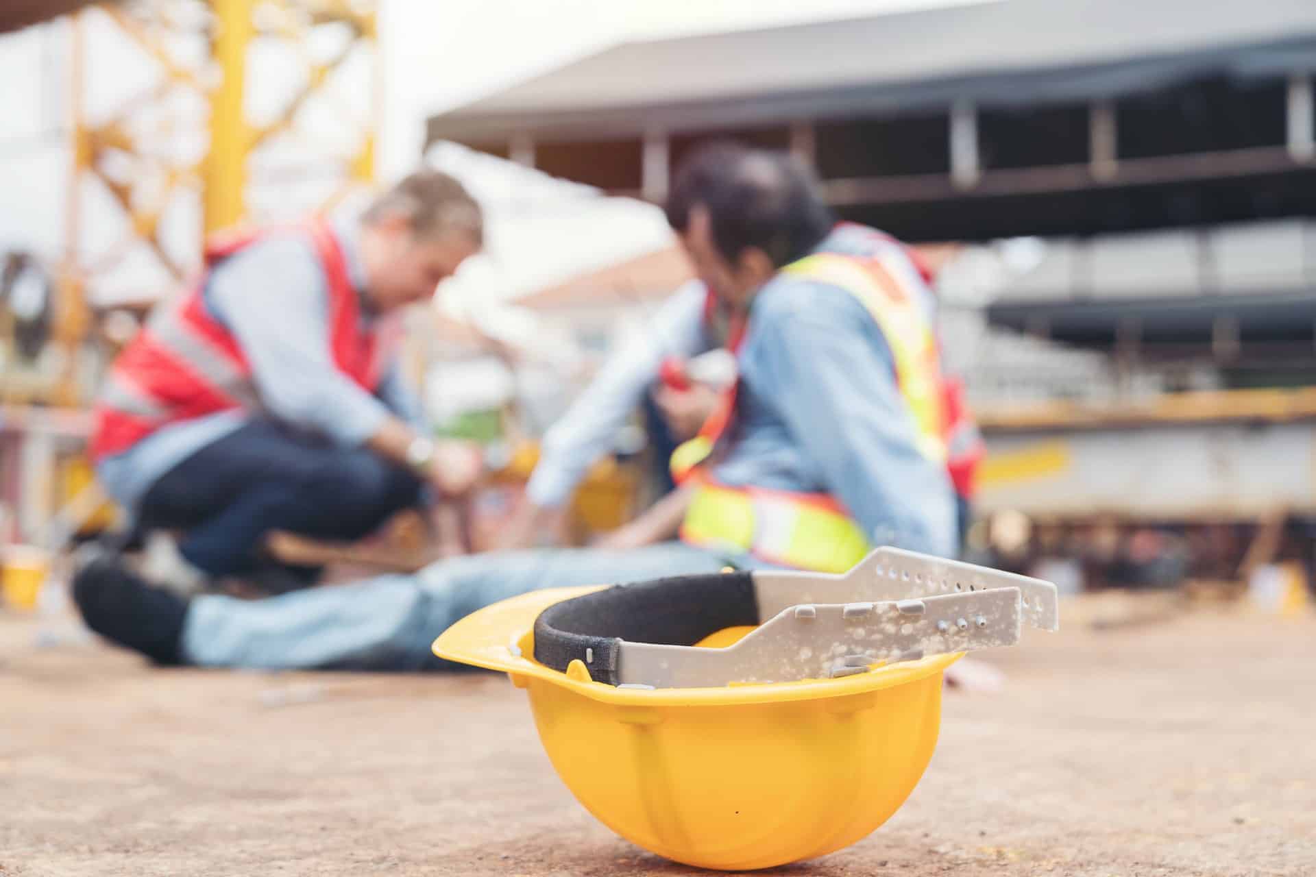 A yellow hardhat with two construction workers in the background