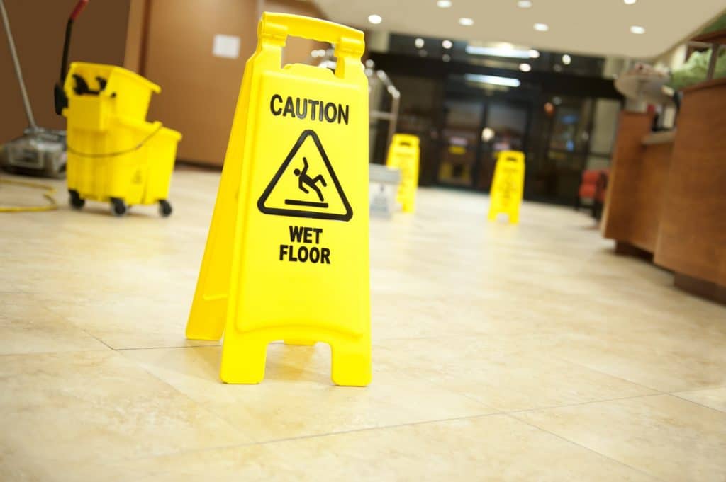 A yellow caution wet floor sign with mop and bucket in background