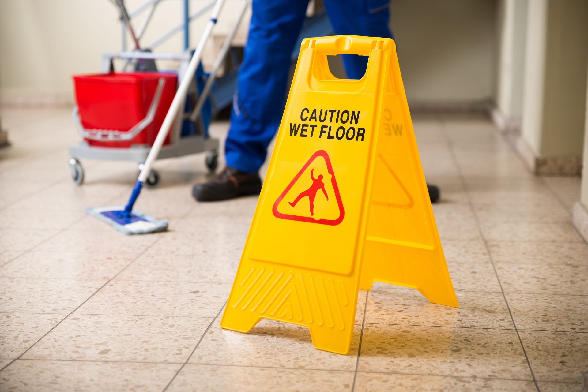 Worker mops with wet floor caution sign | premises liability attorney nyc | Gash & Associates, P.C.