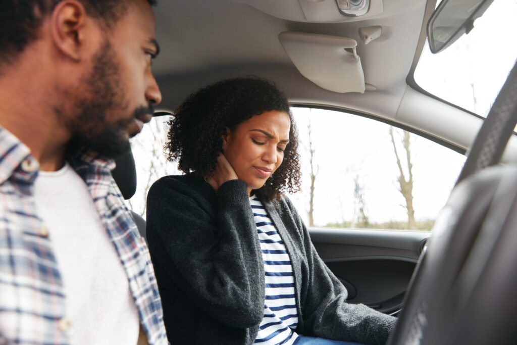 Two people sitting the car and the passenger holding their neck