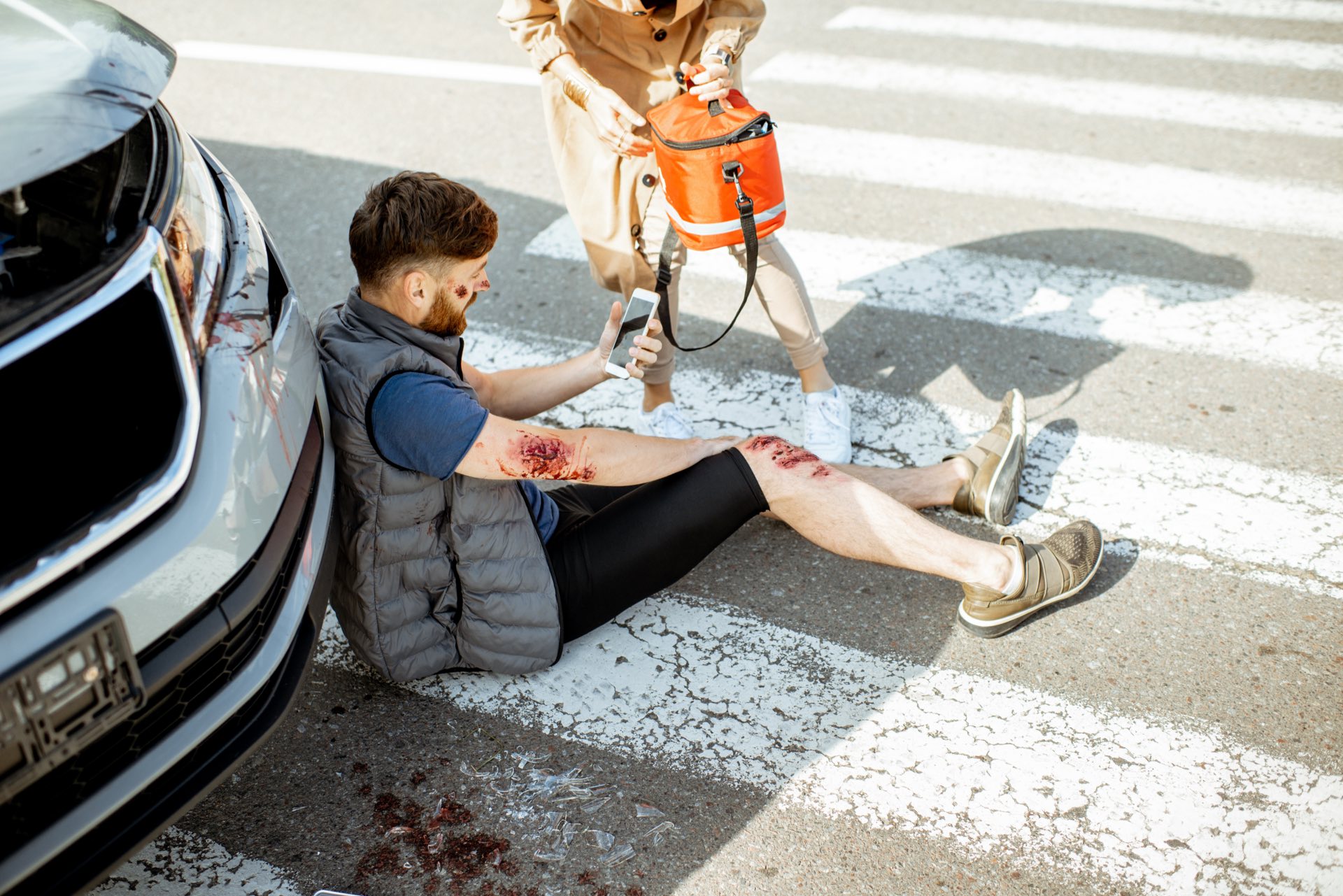 Person sitting in front of a car hurt