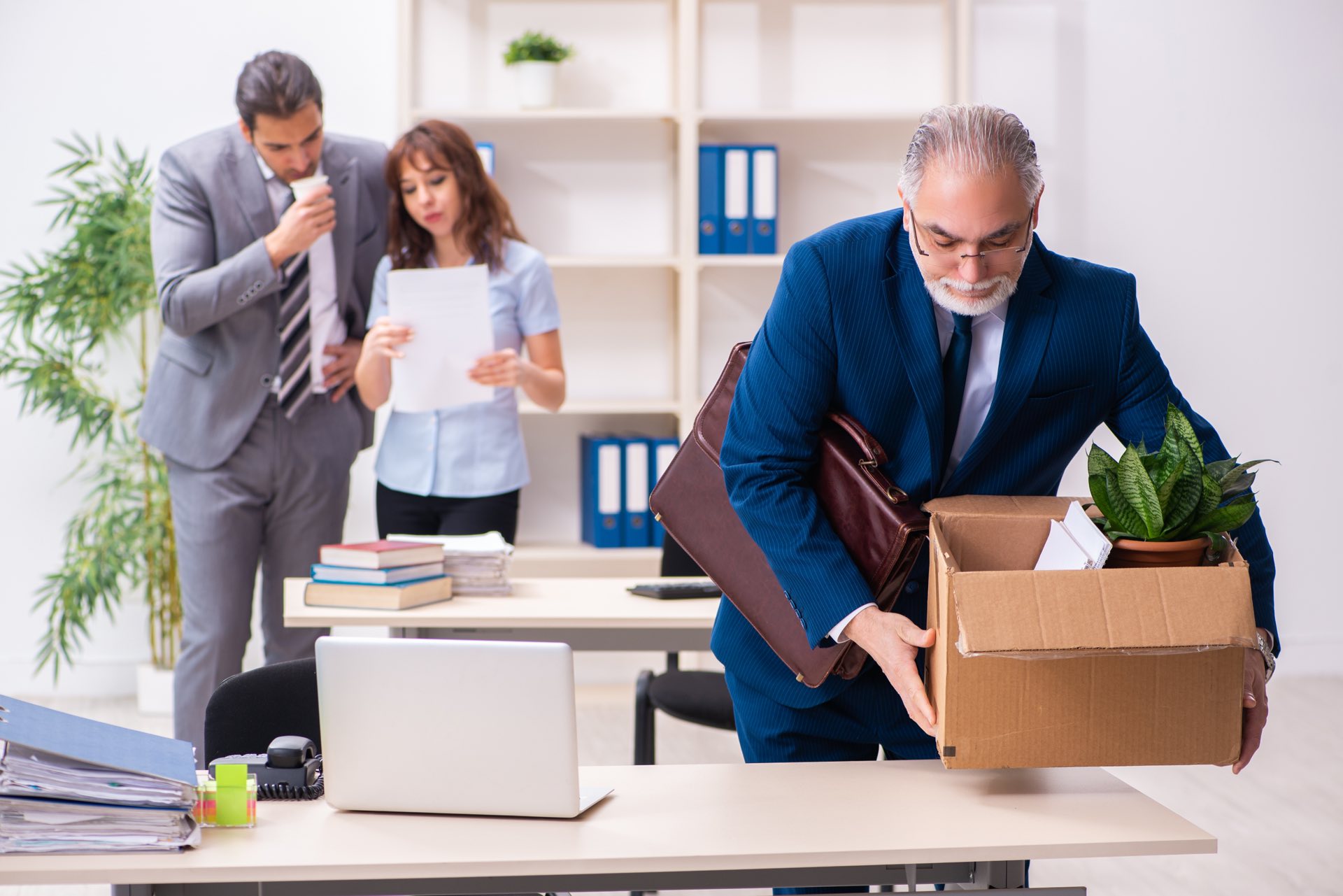 A male and female employee talking while another male employees is packing up his belongings