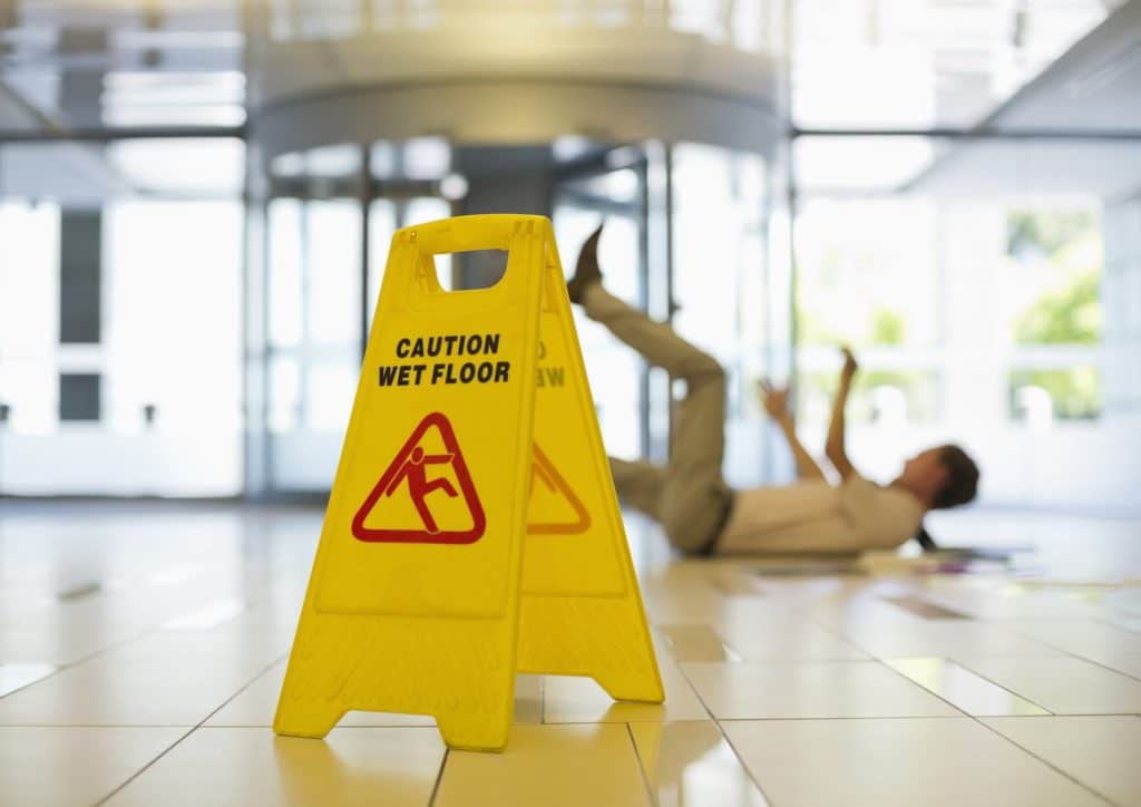 Yellow caution wet floor sign with blurred out fallen man in background