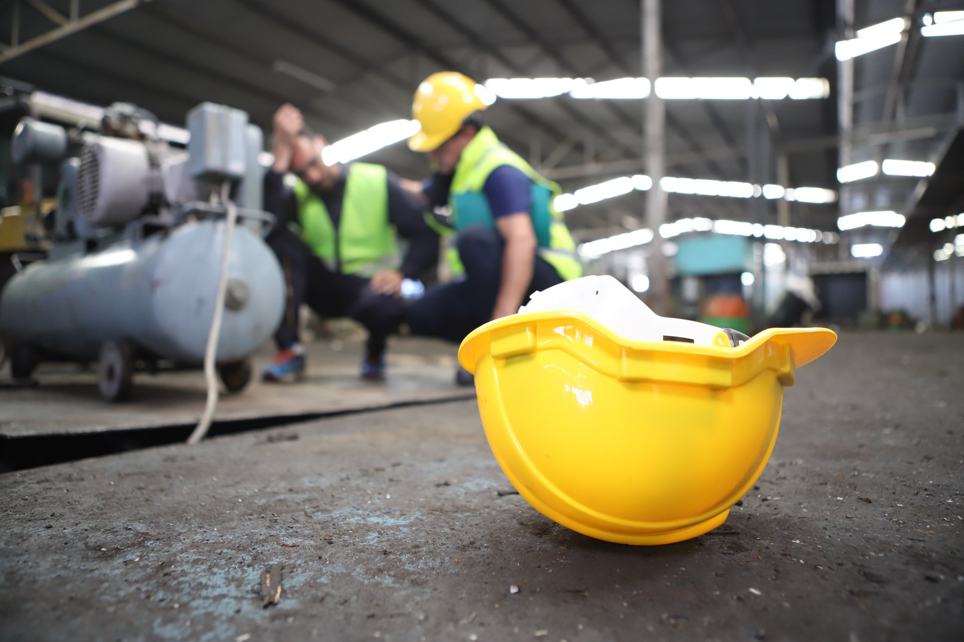 Accident at work of construction worker at site. Safety team helps employee with a yellow hardhat showing