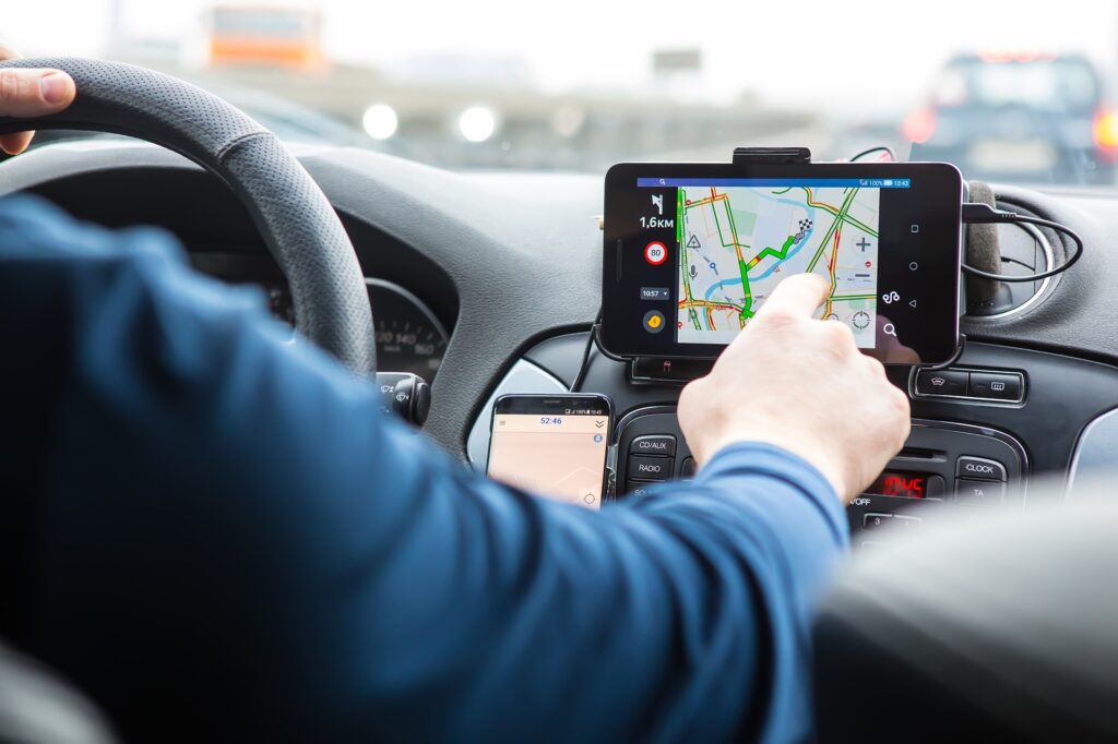 A man behind the wheel in a car interacts with a GPS unit while driving.