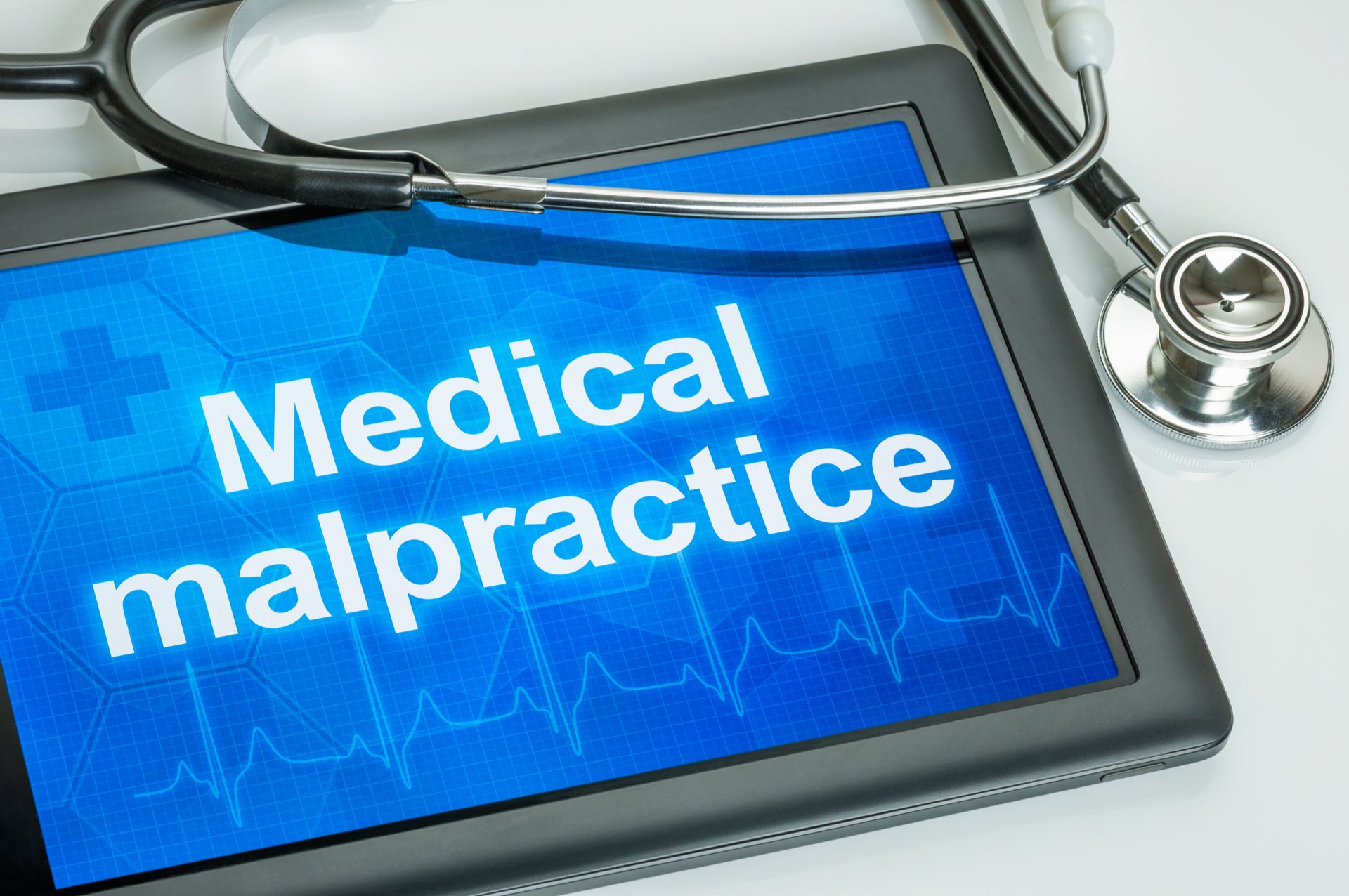 A stethoscope next to an ipad that says Medical malpractice with a blue background