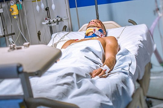 bloodied man in hospital bed with neck brace