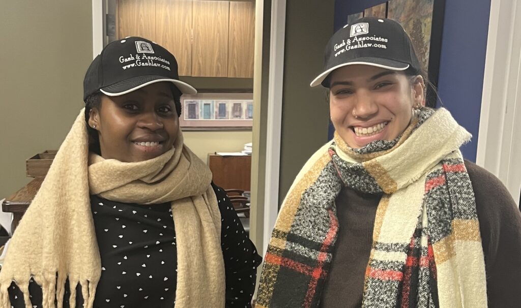 Two female members of staff dressed warmly in hats and scarves and wearing Gash Law baseball caps